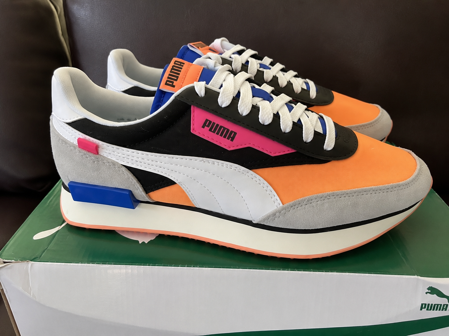 Pair of colorful PUMA sneakers with orange toe caps, black sides, white stripes, and grey suede heel on a green box.