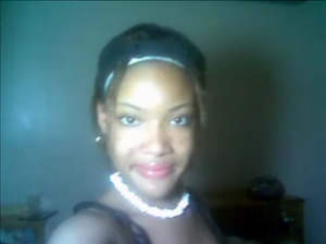 Smiling woman wearing a white headband and pearl necklace, posing for a selfie indoors.