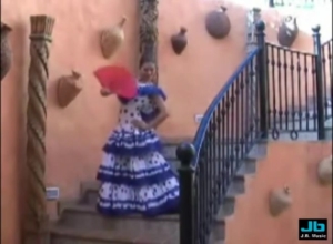 Dancer in a blue and white ruffled dress on a stairway, holding a red fan, with decorative pots on peach-colored walls behind.
