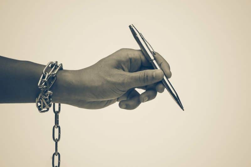 Hand with a chain around the wrist holding a pen, symbolizing censorship or restricted speech