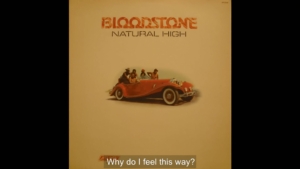 Poster-style image featuring a red vintage convertible with several people riding in it, above which is bold orange typography that reads 'BLOODSTONE', with smaller text 'NATURAL HIGH' underneath. A caption at the bottom says 'Why do I feel this way?' (video still).
